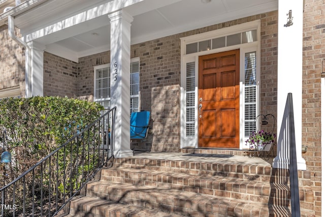 doorway to property featuring covered porch and brick siding