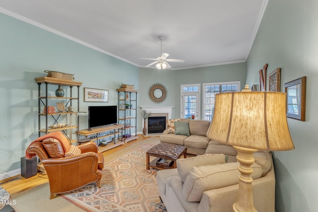 living area featuring crown molding, a glass covered fireplace, ceiling fan, wood finished floors, and baseboards