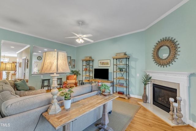 living room featuring ceiling fan, wood finished floors, baseboards, a glass covered fireplace, and crown molding