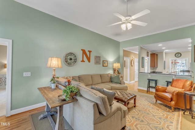 living area with light wood-style floors, a ceiling fan, baseboards, and crown molding