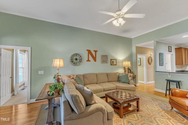 living area with a ceiling fan, light wood-type flooring, ornamental molding, and baseboards