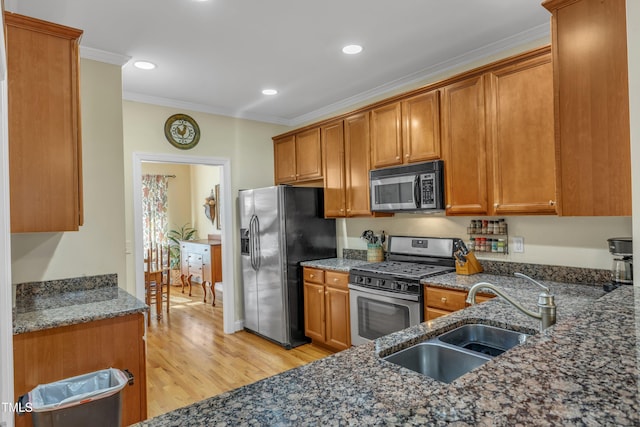 kitchen featuring brown cabinets, dark stone countertops, stainless steel appliances, crown molding, and a sink