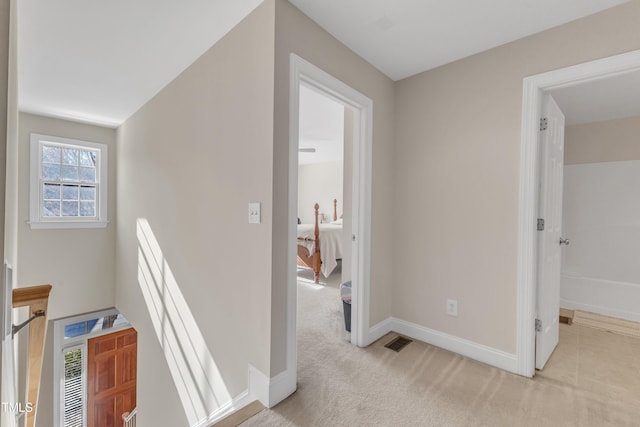 hall featuring visible vents, baseboards, and light colored carpet