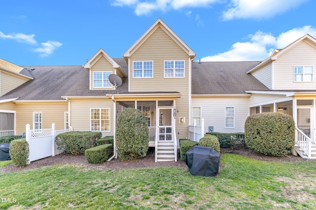 rear view of house featuring a sunroom, a shingled roof, fence, and a lawn