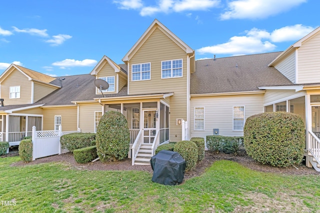 rear view of house featuring a sunroom, a shingled roof, and a lawn