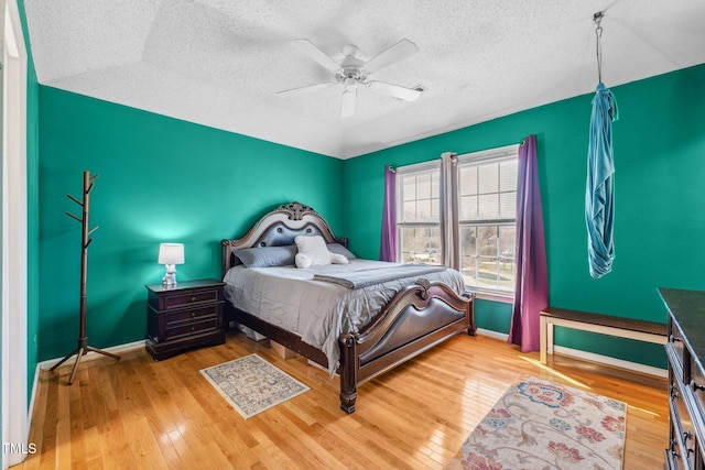 bedroom with baseboards, a textured ceiling, hardwood / wood-style floors, and a ceiling fan