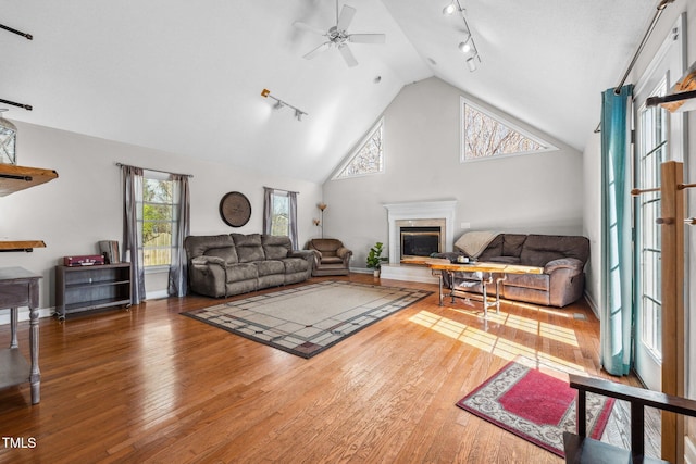 living area with high vaulted ceiling, a high end fireplace, wood-type flooring, rail lighting, and ceiling fan