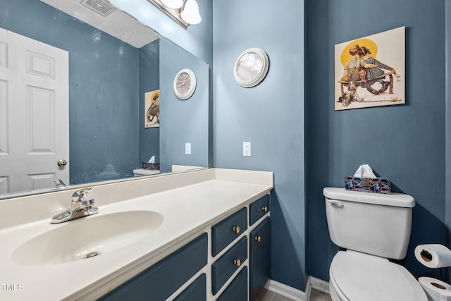 half bathroom with vanity, toilet, baseboards, and visible vents