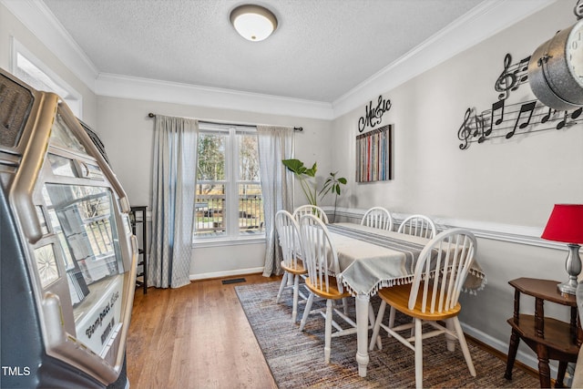 dining space featuring a textured ceiling, wood finished floors, visible vents, and ornamental molding