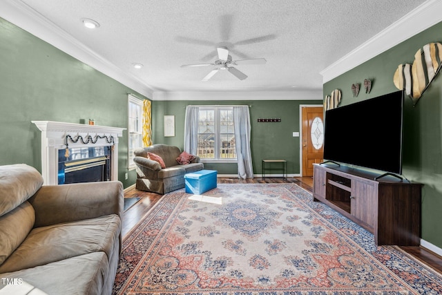 living room with crown molding, baseboards, ceiling fan, a fireplace, and wood finished floors