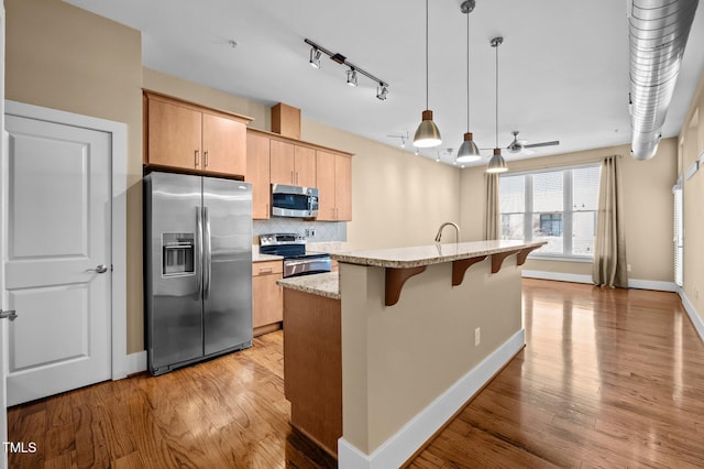 kitchen featuring decorative backsplash, an island with sink, light wood-style flooring, a breakfast bar, and stainless steel appliances