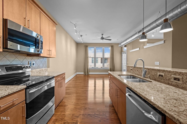 kitchen featuring stainless steel appliances, wood finished floors, a sink, light stone countertops, and tasteful backsplash