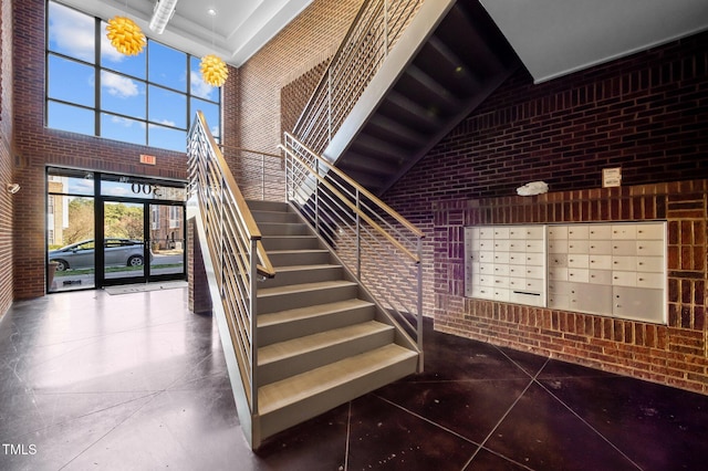 staircase featuring brick wall, a towering ceiling, and mail area