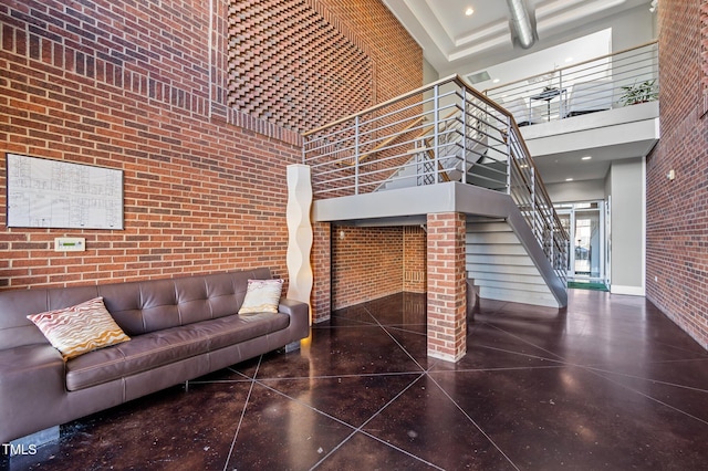 living area featuring a towering ceiling, brick wall, and stairs