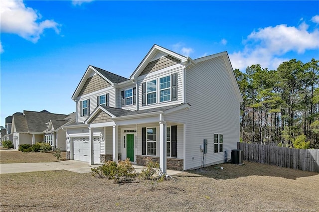 craftsman house featuring central air condition unit, covered porch, concrete driveway, fence, and stone siding