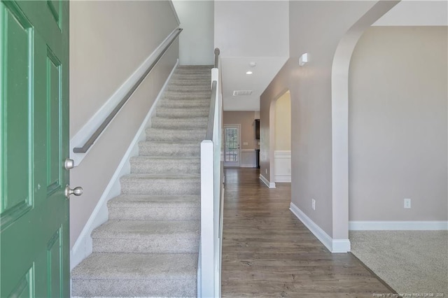 foyer entrance featuring stairs, arched walkways, baseboards, and wood finished floors