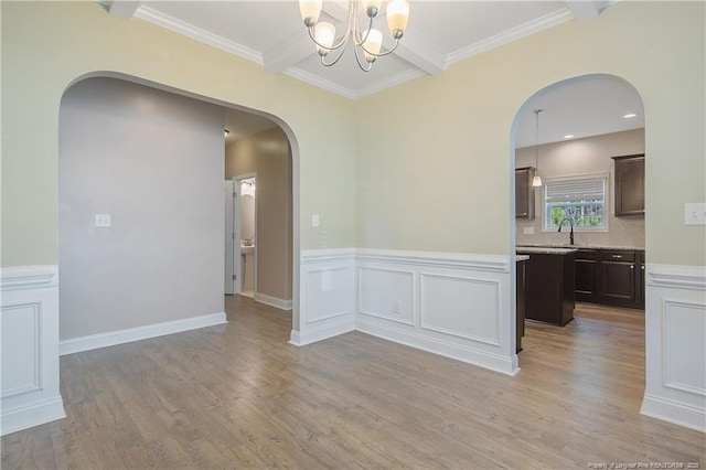 empty room featuring arched walkways, a chandelier, a sink, beam ceiling, and light wood finished floors