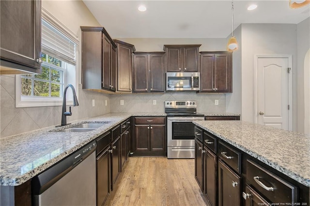 kitchen with dark brown cabinetry, stainless steel appliances, a sink, light wood-style floors, and backsplash