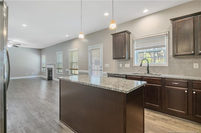 kitchen with a center island, light wood-style flooring, a glass covered fireplace, a sink, and dark brown cabinetry