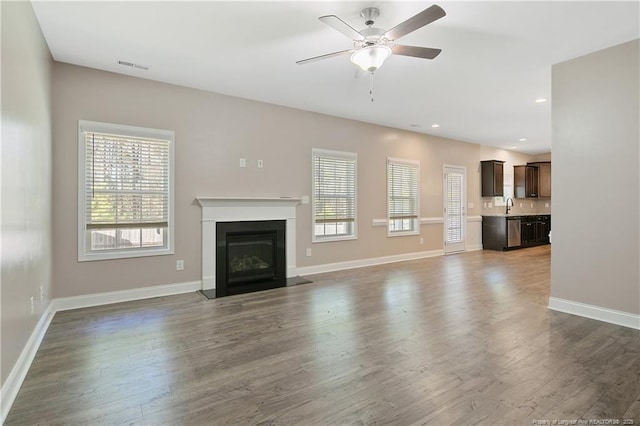 unfurnished living room featuring baseboards, dark wood-style floors, ceiling fan, a fireplace with flush hearth, and a sink