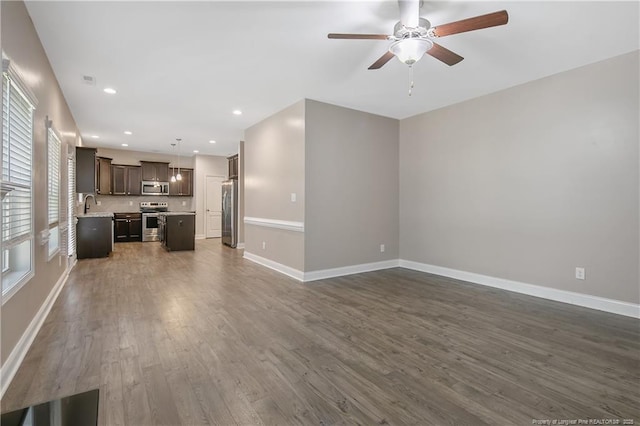 unfurnished living room with ceiling fan, recessed lighting, a sink, baseboards, and dark wood finished floors