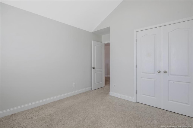 unfurnished bedroom with carpet floors, a closet, vaulted ceiling, and baseboards