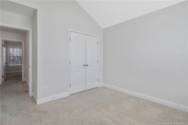 unfurnished bedroom with carpet floors, lofted ceiling, a closet, and baseboards