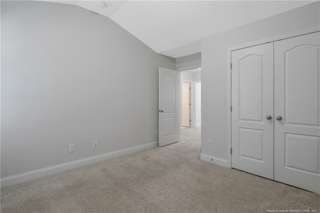 unfurnished bedroom featuring a closet, light carpet, vaulted ceiling, and baseboards