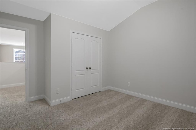 unfurnished bedroom with carpet, baseboards, vaulted ceiling, and a closet