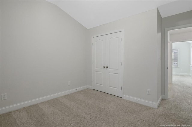 unfurnished bedroom featuring carpet floors, baseboards, vaulted ceiling, and a closet