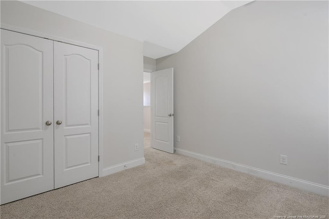 unfurnished bedroom with a closet, light colored carpet, vaulted ceiling, and baseboards