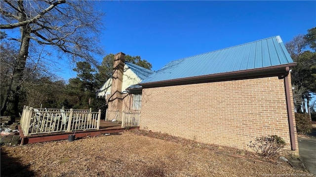 view of property exterior featuring metal roof, brick siding, a chimney, and a wooden deck