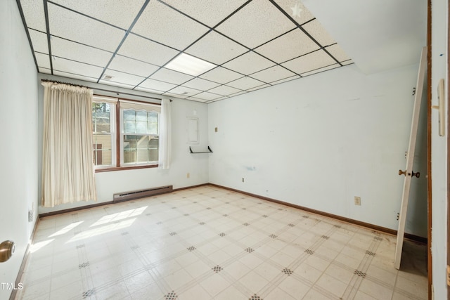 unfurnished room with a baseboard heating unit, baseboards, a paneled ceiling, and tile patterned floors