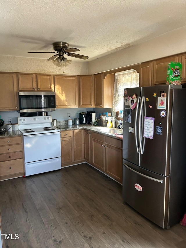 kitchen featuring brown cabinetry, a ceiling fan, appliances with stainless steel finishes, dark wood-style flooring, and a textured ceiling