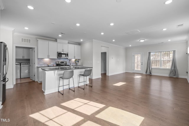 kitchen with washing machine and clothes dryer, visible vents, tasteful backsplash, appliances with stainless steel finishes, and a kitchen island with sink