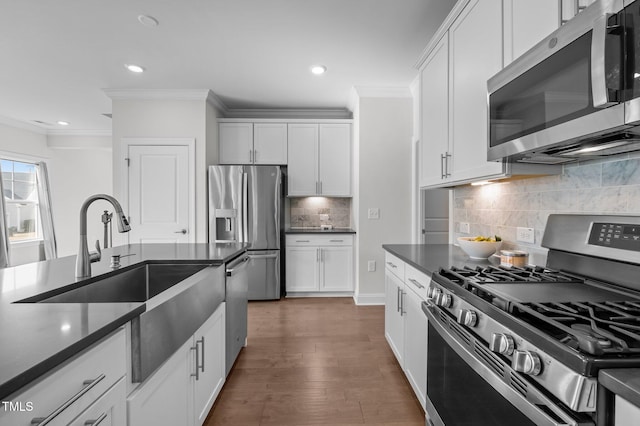 kitchen with dark countertops, a sink, crown molding, appliances with stainless steel finishes, and dark wood-style flooring