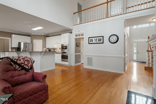 living room featuring ornamental molding, a high ceiling, visible vents, and light wood-style floors