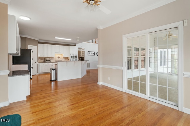 unfurnished living room with light wood finished floors, ornamental molding, a ceiling fan, and baseboards