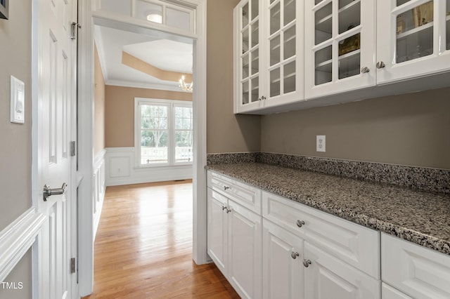 kitchen with a wainscoted wall, light wood finished floors, ornamental molding, stone countertops, and white cabinets