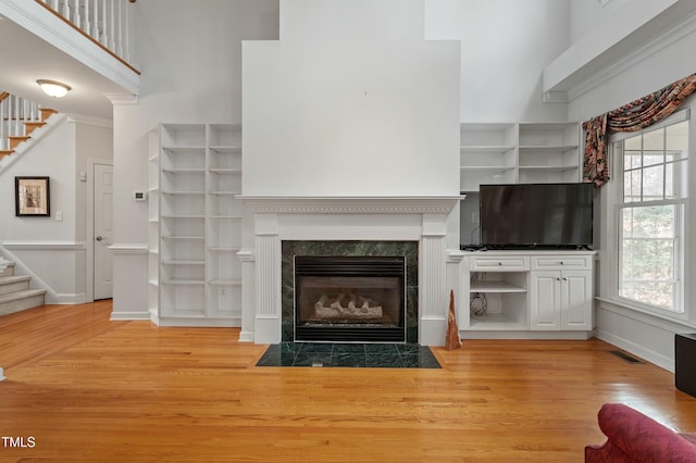 unfurnished living room featuring stairs, a high ceiling, a fireplace, and light wood-style flooring