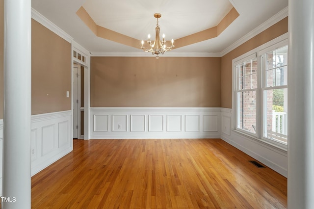 spare room featuring light wood finished floors, visible vents, a raised ceiling, a wainscoted wall, and an inviting chandelier