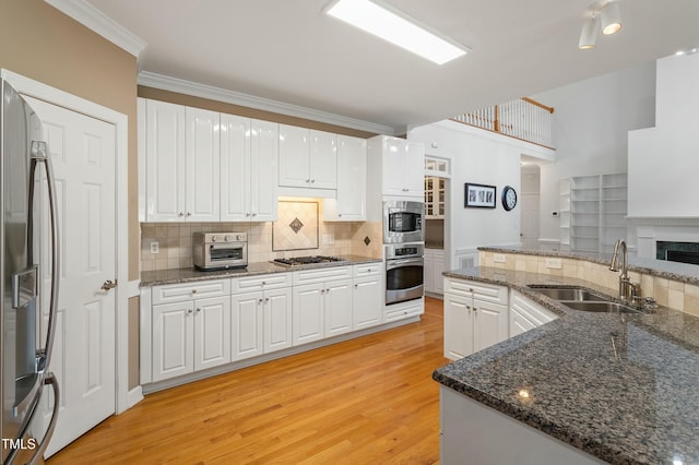 kitchen featuring light wood finished floors, appliances with stainless steel finishes, crown molding, white cabinetry, and a sink