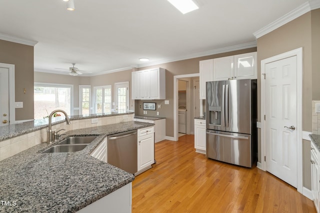 kitchen featuring washer / dryer, stainless steel appliances, light wood-type flooring, white cabinetry, and a sink