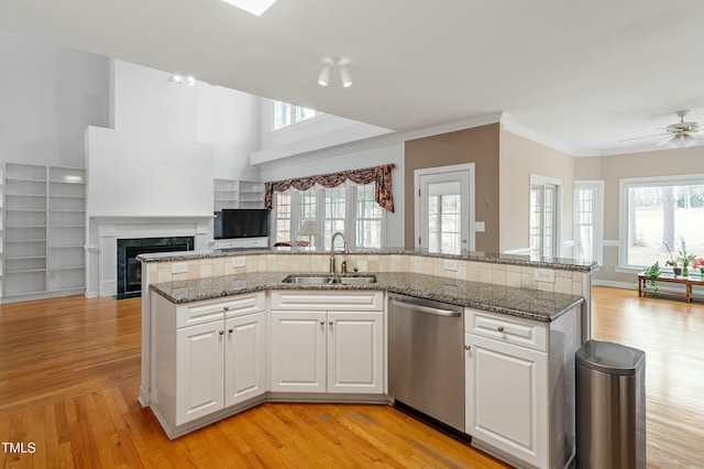 kitchen featuring a sink, a high end fireplace, open floor plan, dishwasher, and light wood finished floors