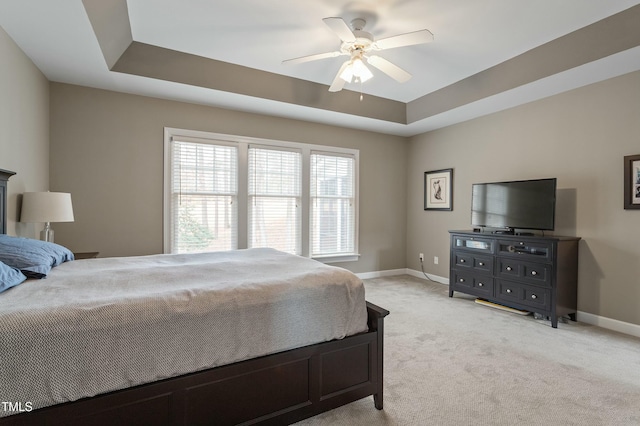 bedroom featuring light carpet, ceiling fan, a tray ceiling, and baseboards