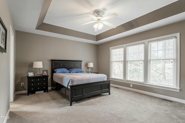 bedroom with baseboards, visible vents, a tray ceiling, and light colored carpet