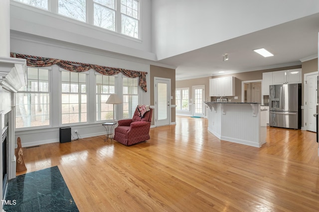 unfurnished living room with ornamental molding, light wood-type flooring, a fireplace with flush hearth, and baseboards