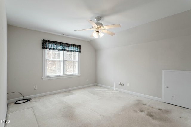 carpeted spare room with a ceiling fan, vaulted ceiling, and baseboards