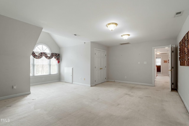 empty room featuring lofted ceiling, light colored carpet, visible vents, and baseboards