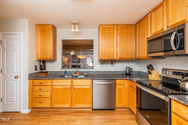 kitchen featuring stainless steel appliances, light wood finished floors, dark stone countertops, and a sink